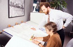 A man and woman working at a drafting table, reviewing plans.